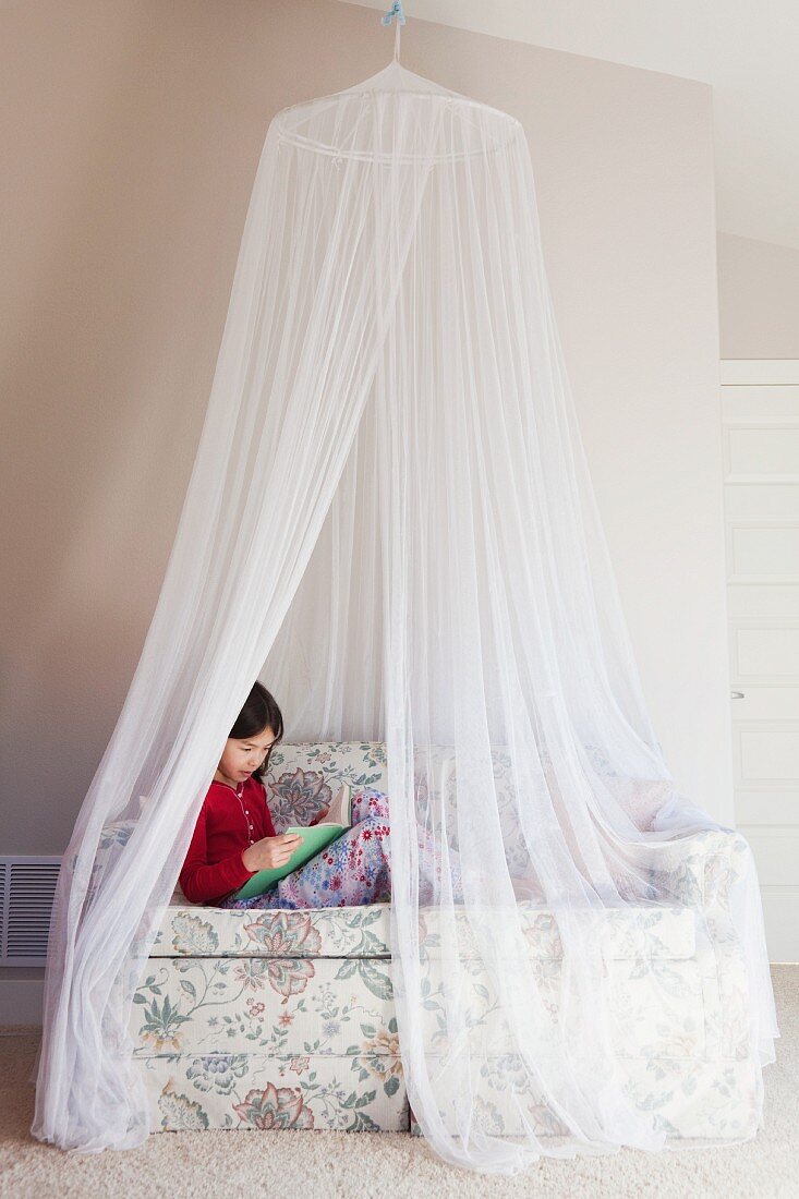 Girl sitting on sofa under mosquito net reading
