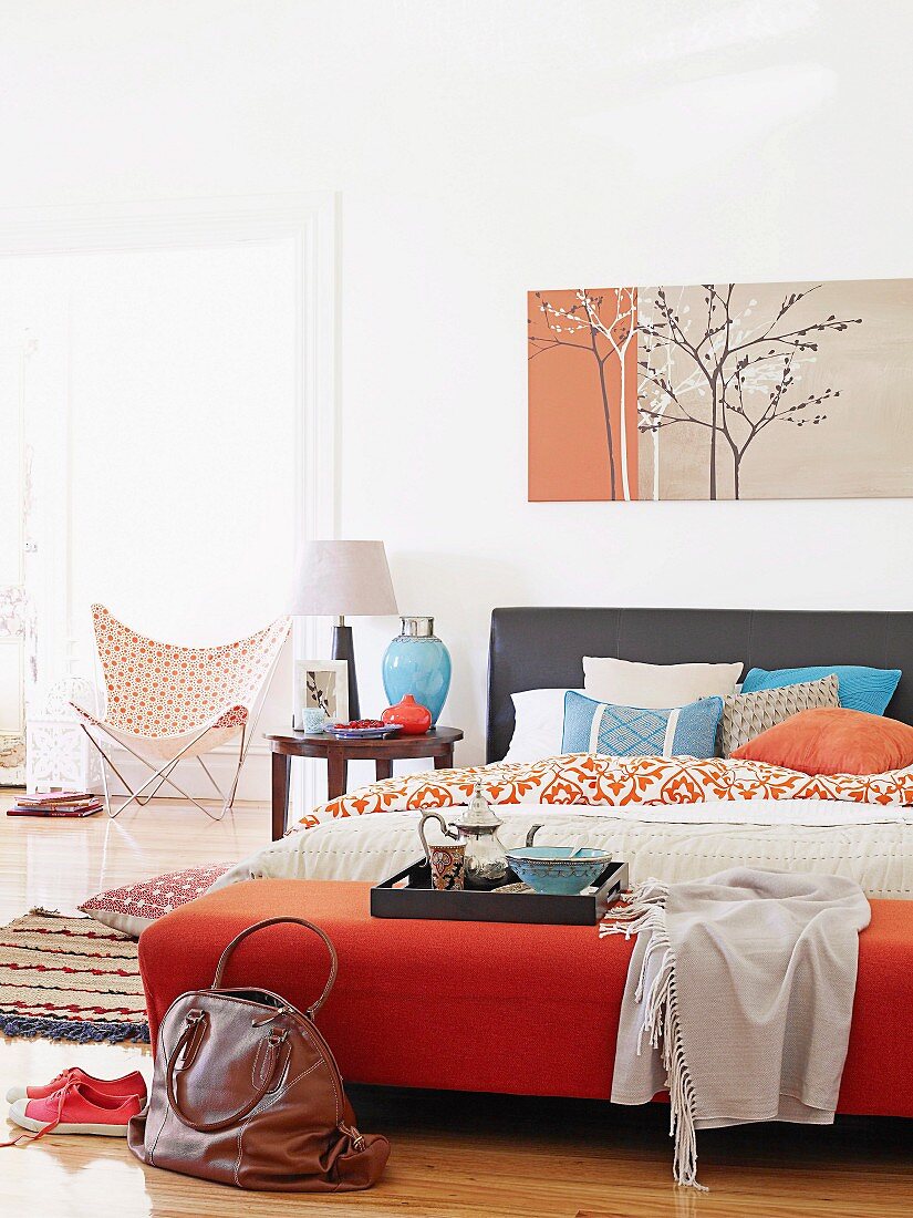 Großes Doppelbett unter Wandbild mit filigranem Baummotiv; auf dem Bett ein Frühstückstablett mit silberner Kanne und versilberter Essschale