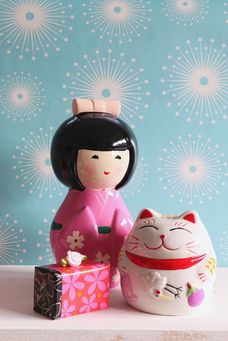 Japanese doll money box, Oriental lucky cat and gift box against pale blue wallpaper