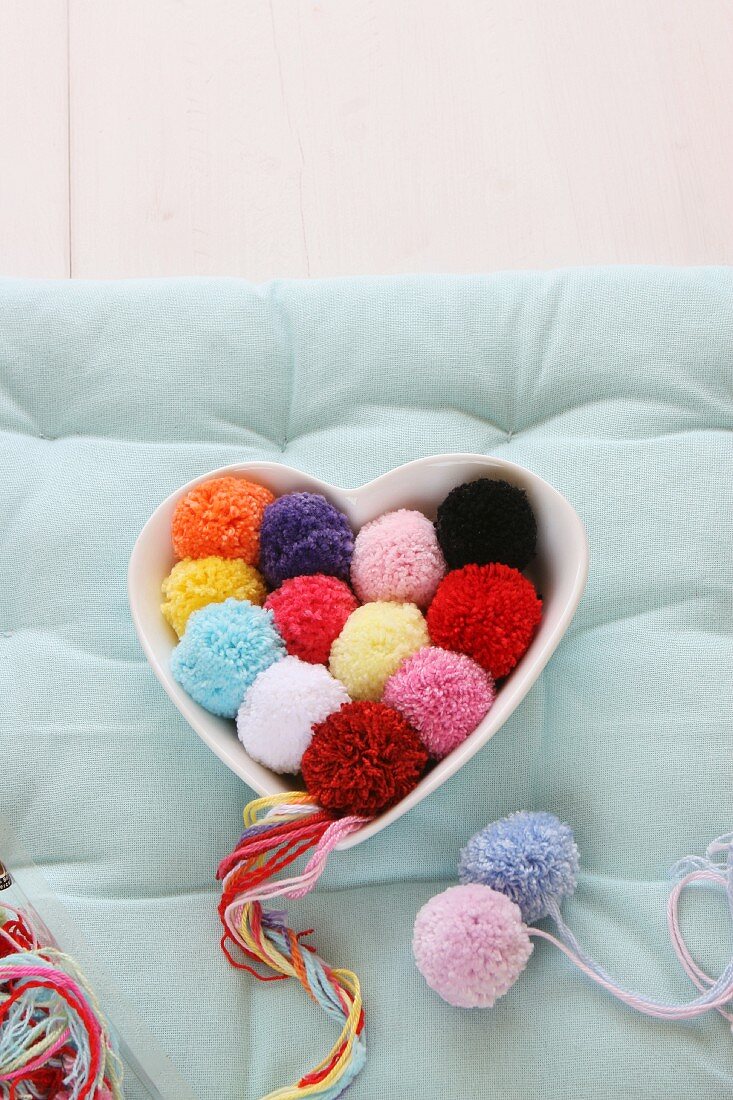 Pompoms of various colours in heart-shaped china dish
