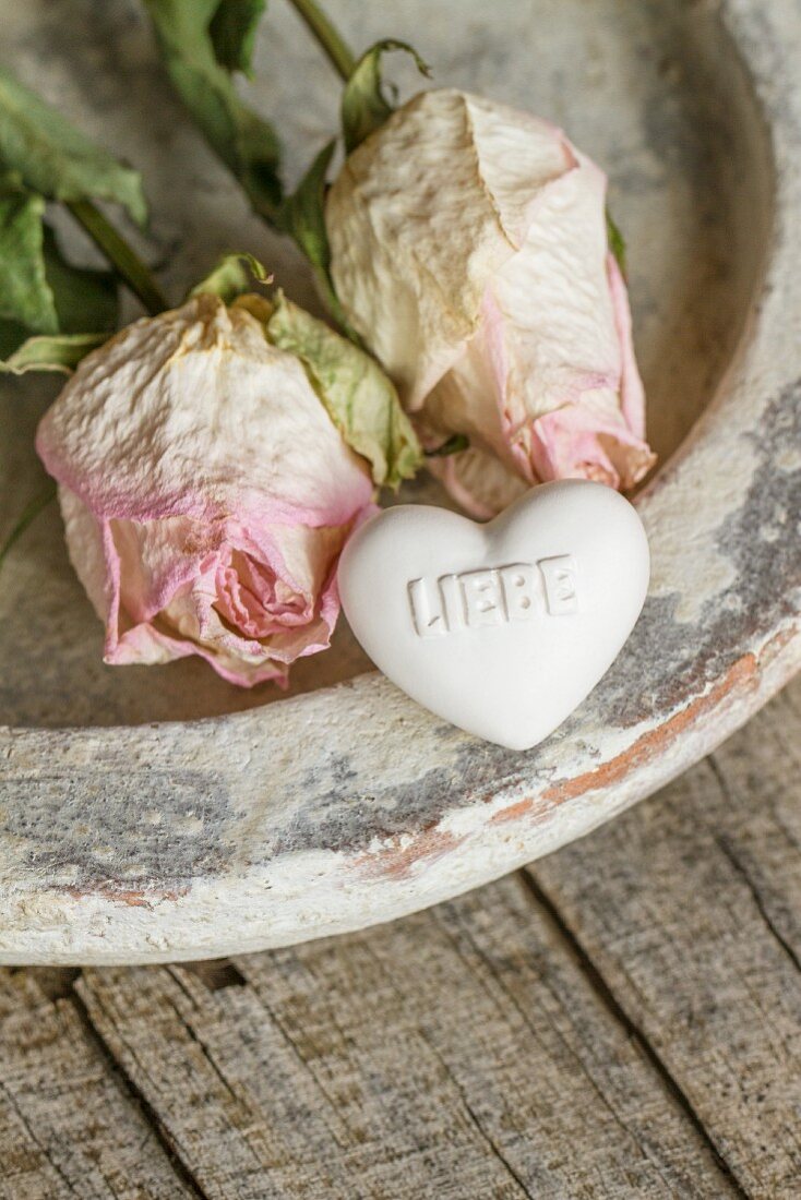 Two dried roses and heart-shaped soap with love message on vintage clay dish