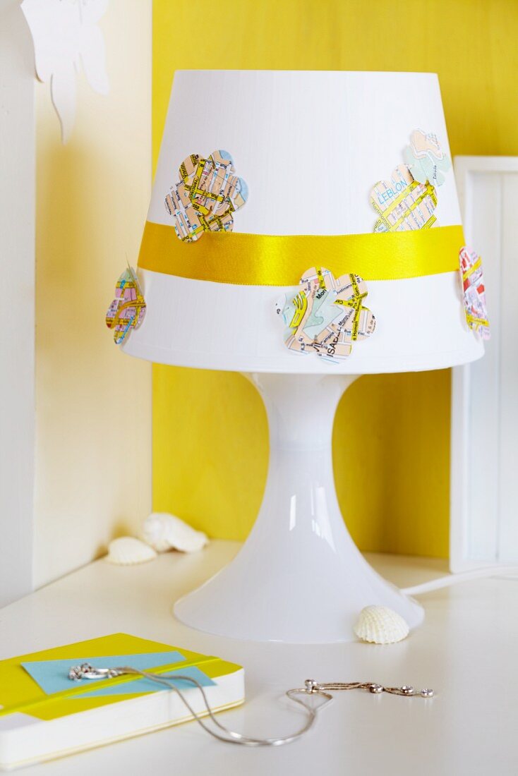 Flower-shapes cut from map and golden ribbon decorating lampshade