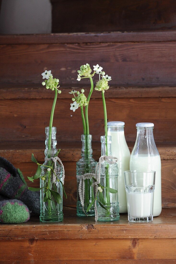 Old glass bottles with Star-of-Bethlehem flowers and full milk bottles on wooden steps