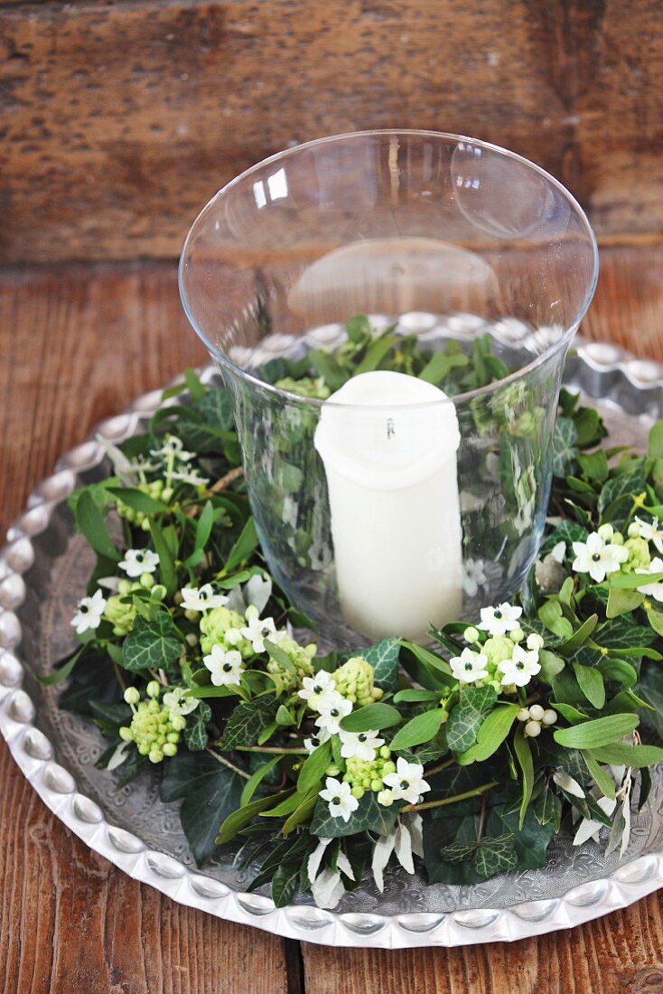Candle in lantern surrounded by wreath of Star-of-Bethlehem flowers and mistletoe on silver-coloured tray