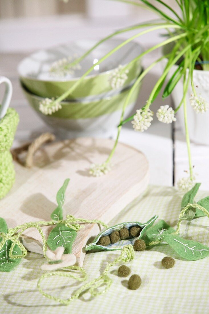 Spring arrangement with felt pea pods on table set with wooden boards and cereal bowls