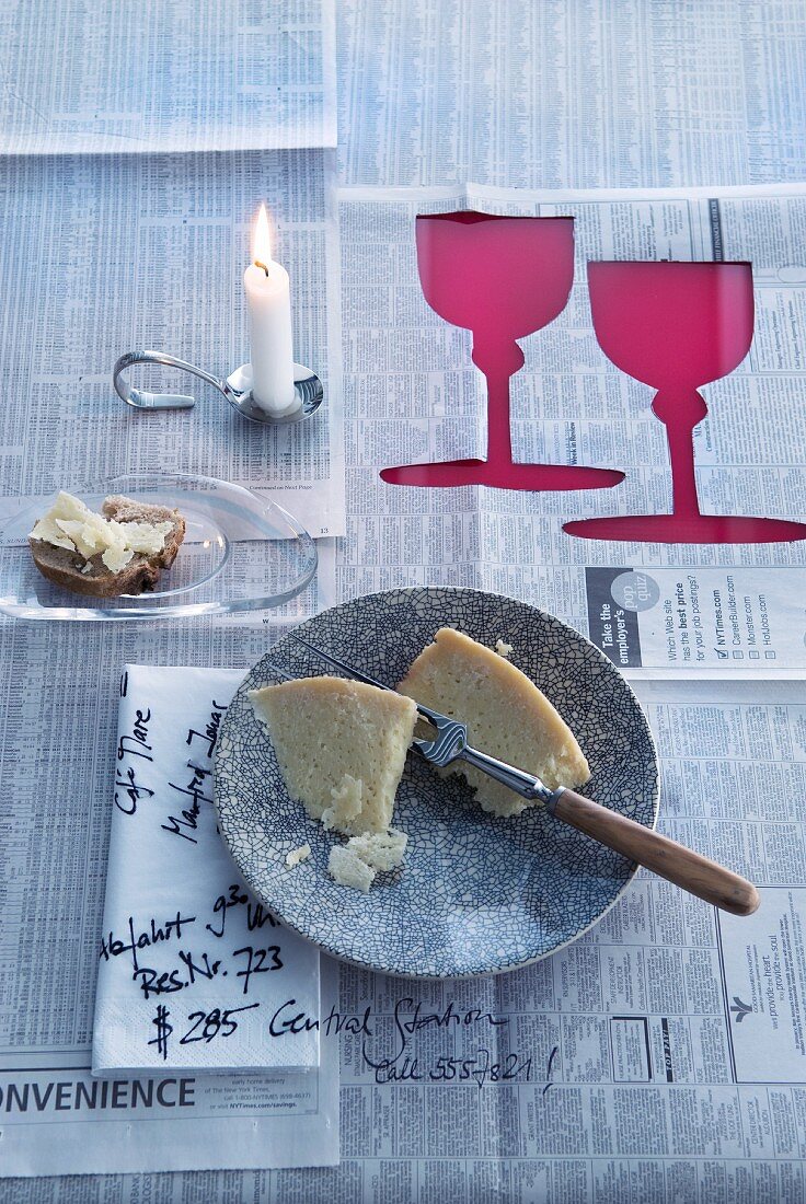 Tischdecke aus Zeitungspapier mit ausgeschnittenen Weinglas-Silhouetten, bekritzelter Serviette und Kerzenhalter in Löffelform