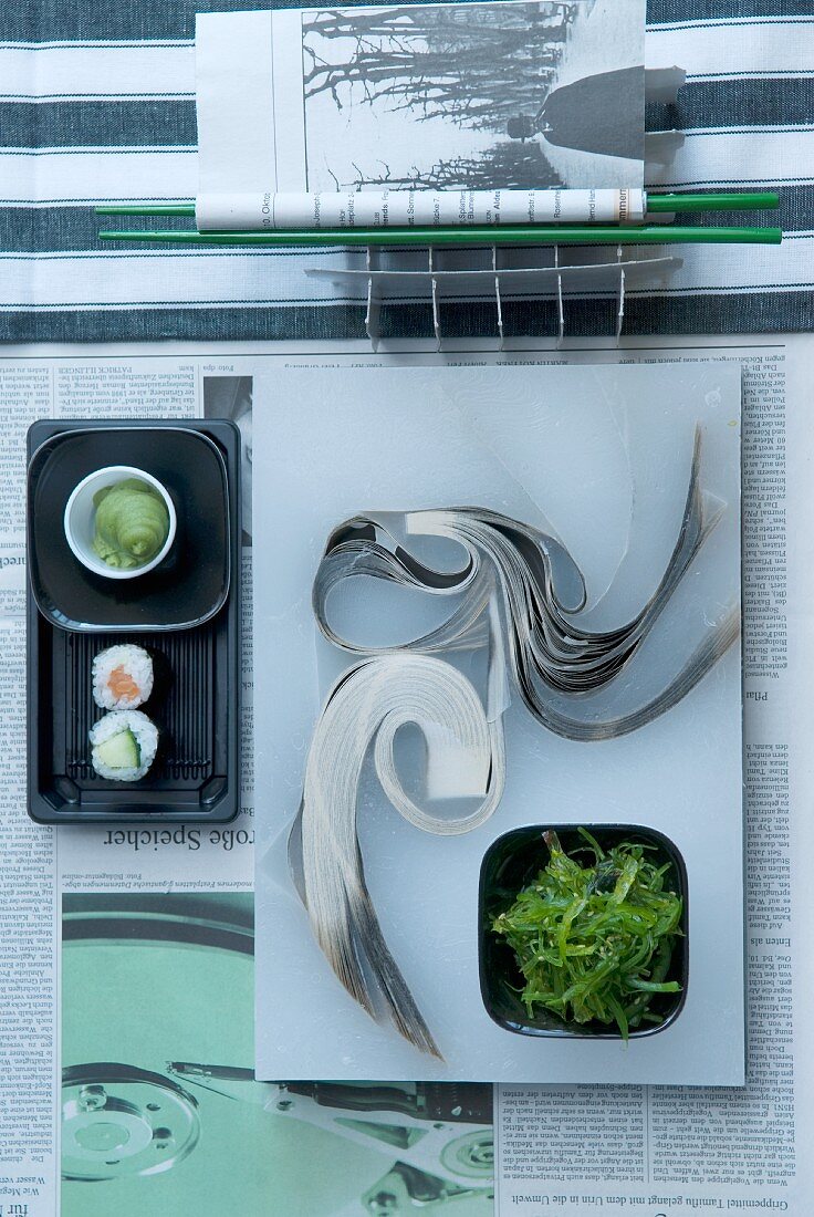Moderne asiatische Tischdeko mit Sushi und Algensalat auf Zeitung