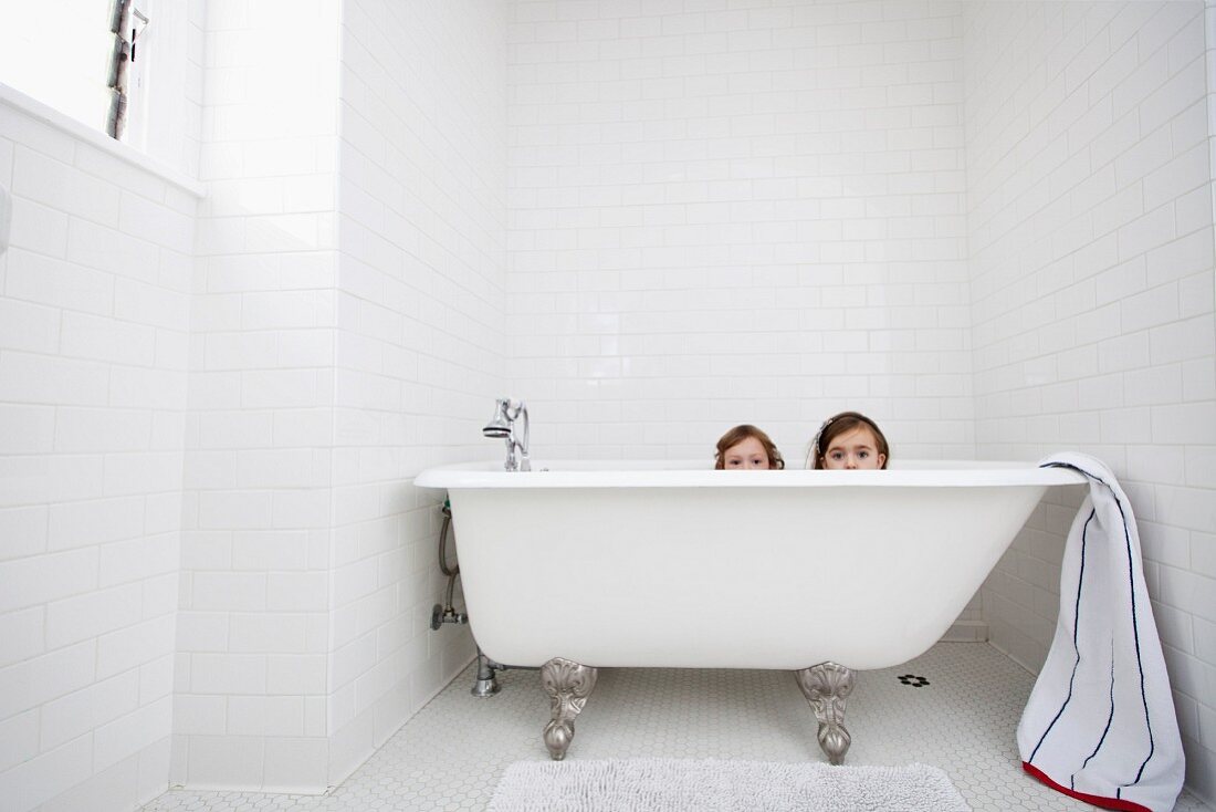 Zwei kleine Mädchen lugen über den Rand einer Retro Badewanne