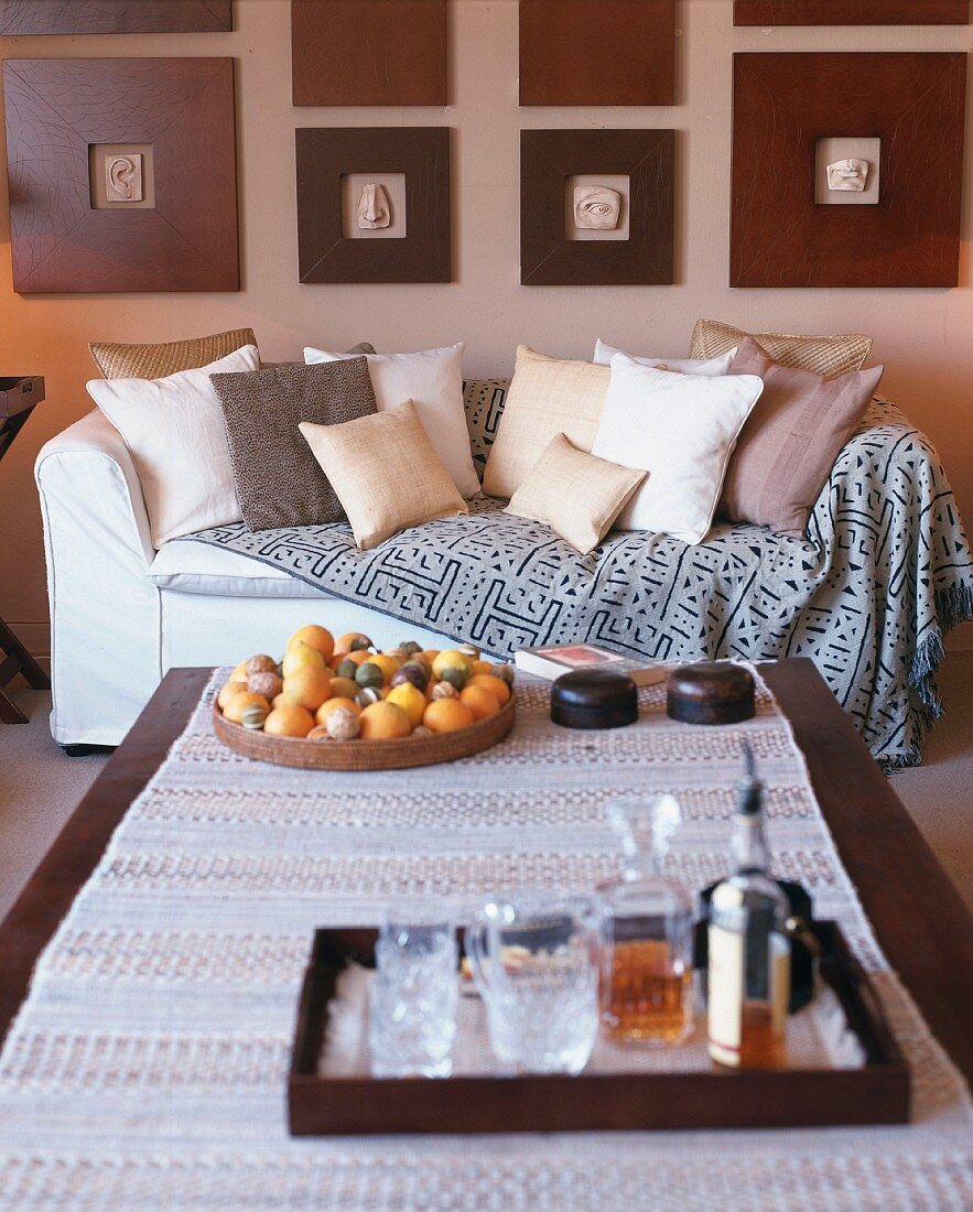 Naturtöne in Wohnraum mit zeitgenössischen Reliefs in breiten Holzrahmen über einem Sofa; Tabletts mit Drinks und Früchten auf Couchtisch im Vordergrund