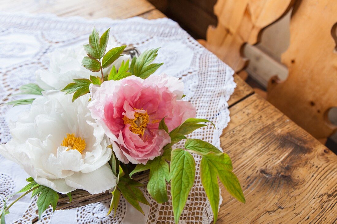 Zwei Pfingstrosenblüten in Körbchen als Deko auf rustikalem Holztisch