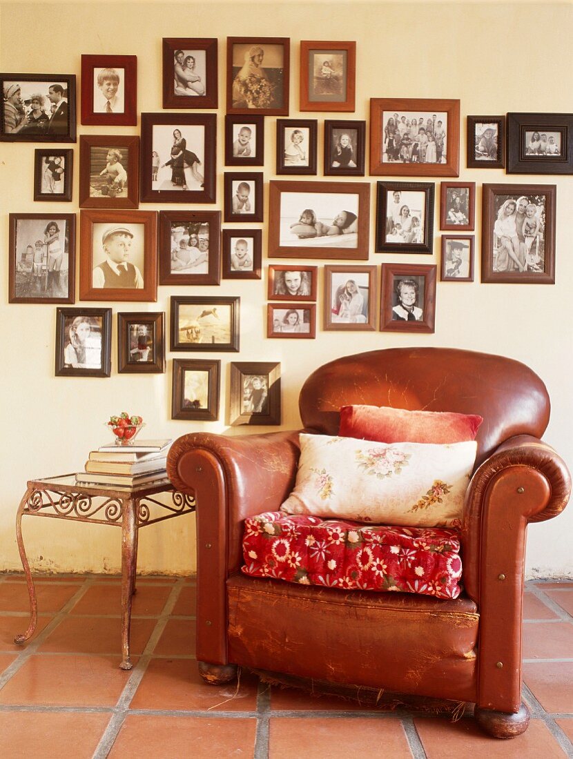Old, brown leather armchair and side table below collection of framed photos on wall
