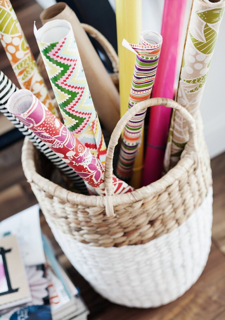 Rolls of colourful, patterned wrapping paper in white basket
