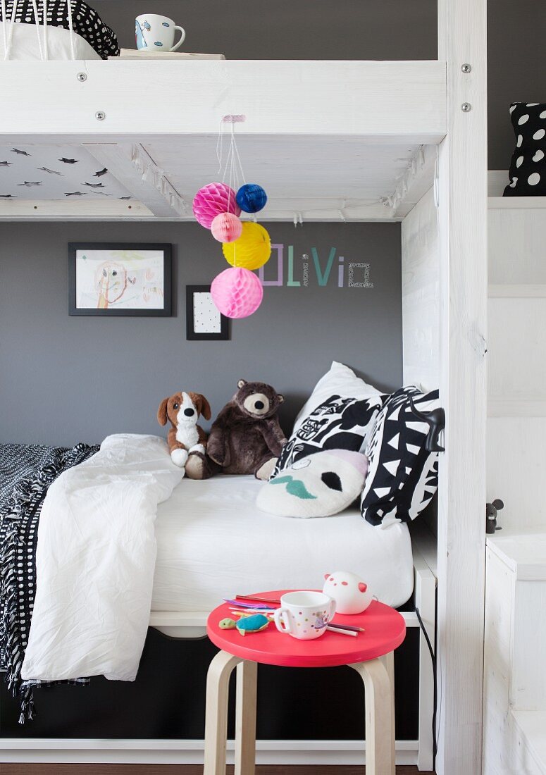 Bunk beds with soft toys and black and white bed linen against mid-grey wall and stool with pink seat in foreground
