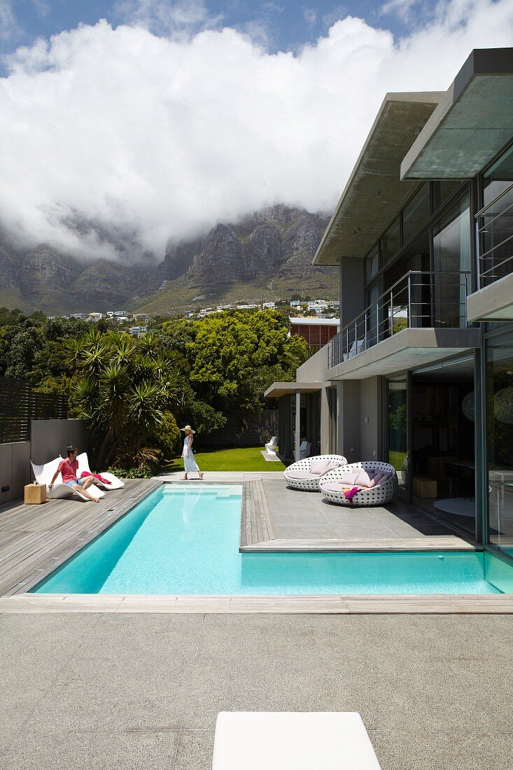 Modernes Luxushaus in Beton mit L-förmigem Pool, Terrasse, Garten und weißen Wolken am blauen Himmel