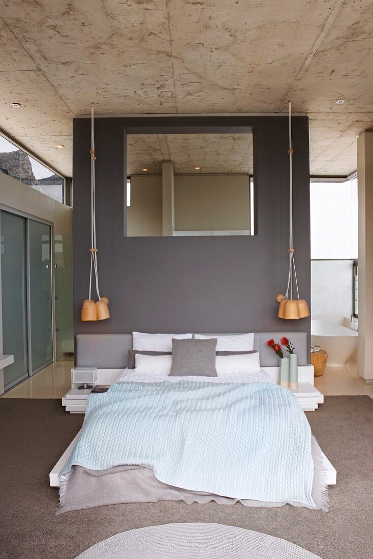 Elegantes puristisches Designerschlafzimmer mit grauer Wandscheibe und Wandspiegel, Zugang zur Bad-Ensuite