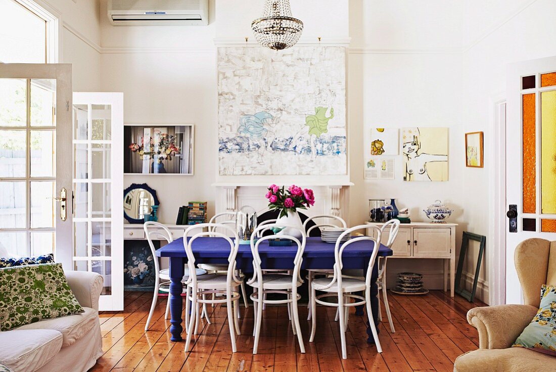 Rustic interior with white-painted Thonet chairs, deep blue dining table, pictures on wall and French windows to one side