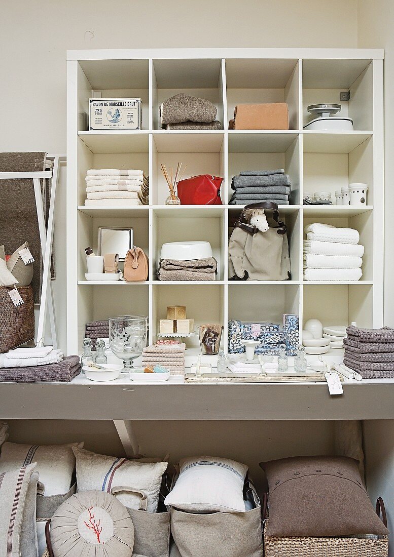 Home accessories in sales room - linen textiles, cushions and crockery stacked on shelves and on floor