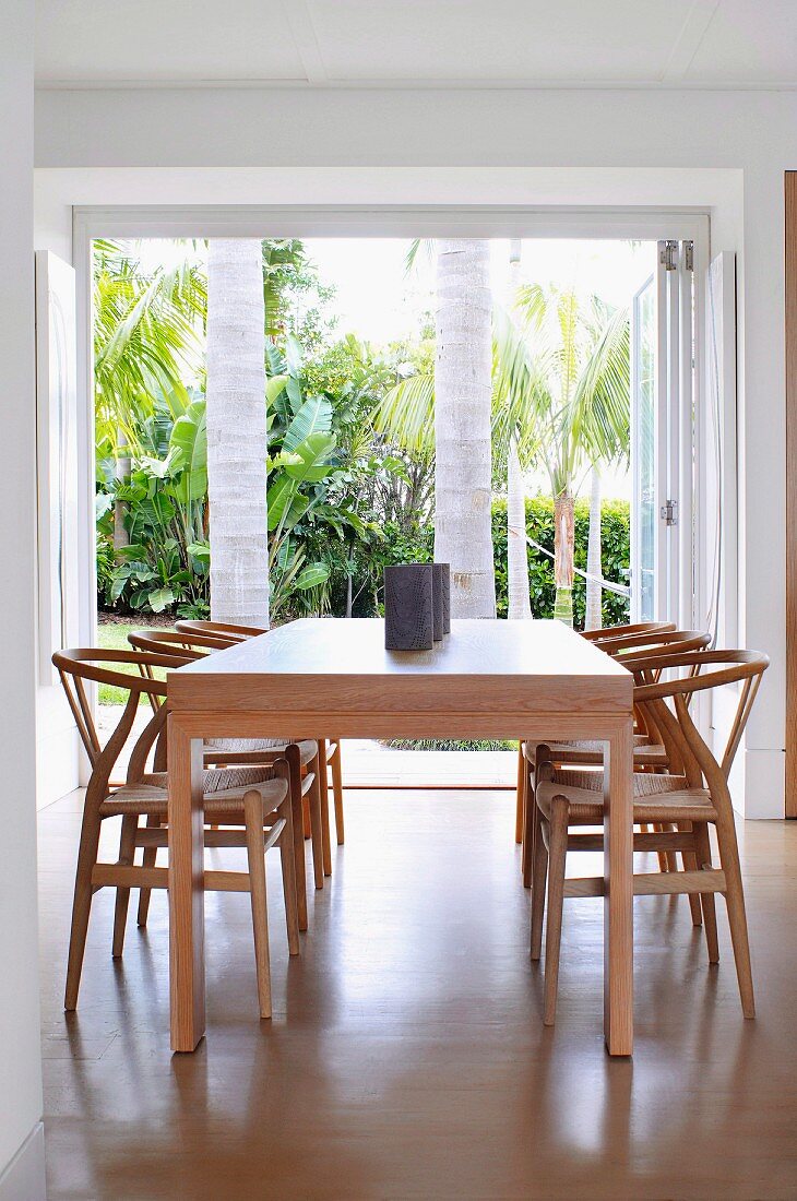 Schlichter eleganter Holztisch mit Hans Wegner Holzstühlen und Gartenblick mit Palmen