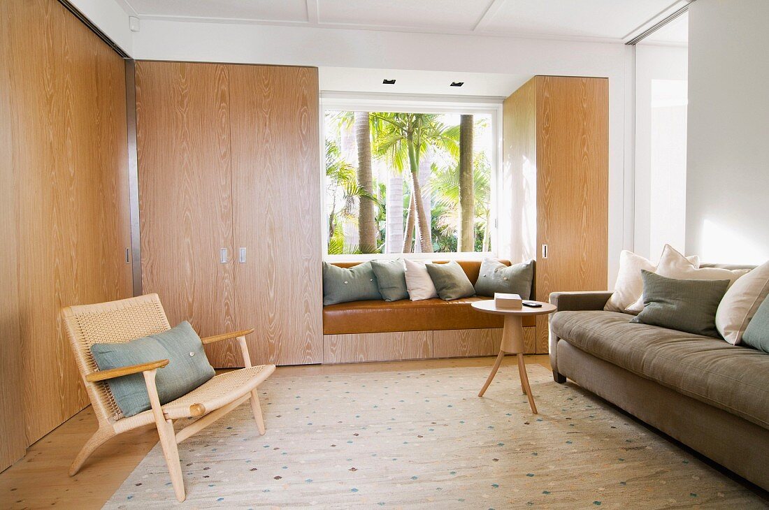 Schlichte raumhohe Einbauschränke mit Holzmaserung im Loungebereich mit eingebauter Sitznische vor Verglasung mit Gartenblick