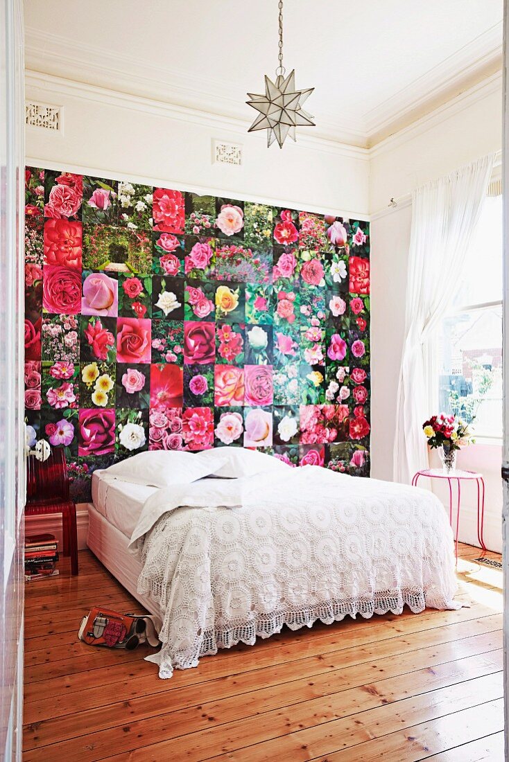 Double bed with white lace bedspread against wall covered in pictures of flowers in rustic interior