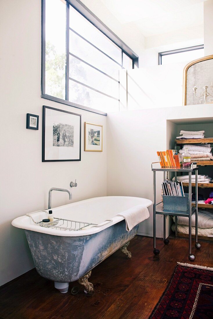 Vintage bathtub below window and fitted partition elements in loft apartment in renovated industrial building