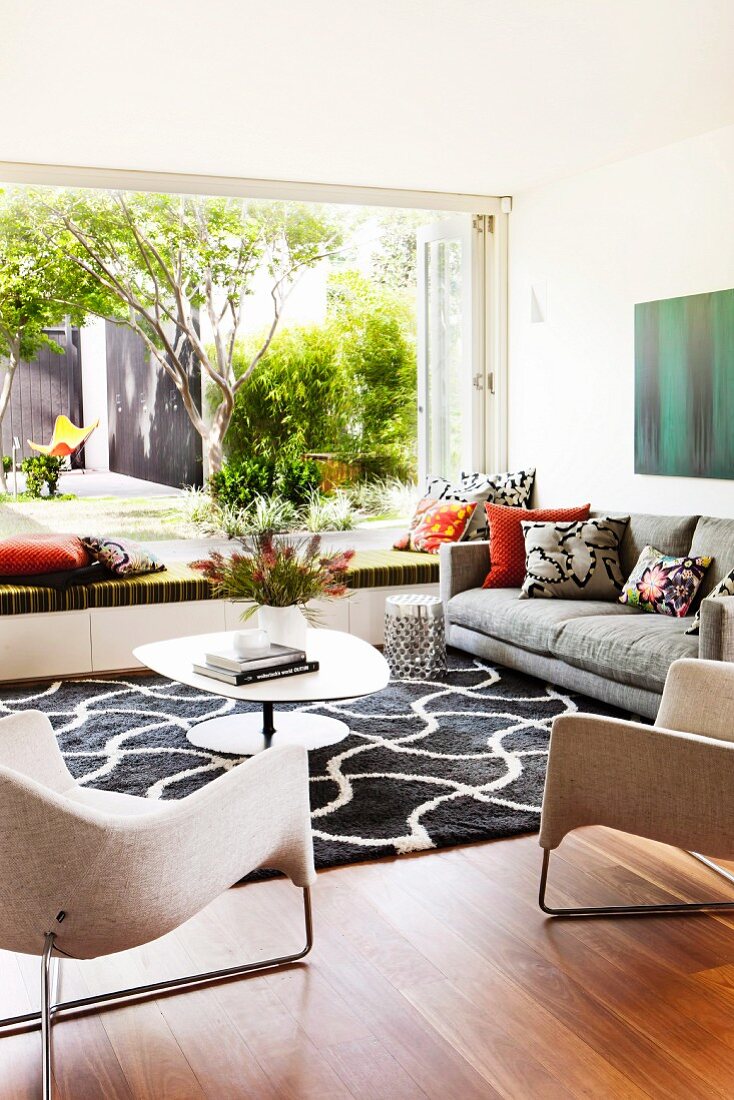 Stilvolles Wohnzimmer mit Designermöbeln und grafischem Teppichmuster in schwarz-weiß, geöffnete Fenster und Blick in sommerlichen Garten