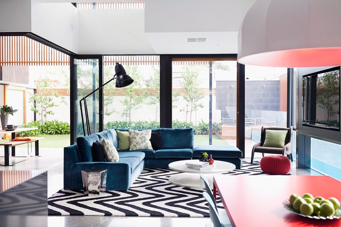 Open terrace doors, black and white zig-zag rug and comfortable grey-blue sofa set in retro, open-plan interior