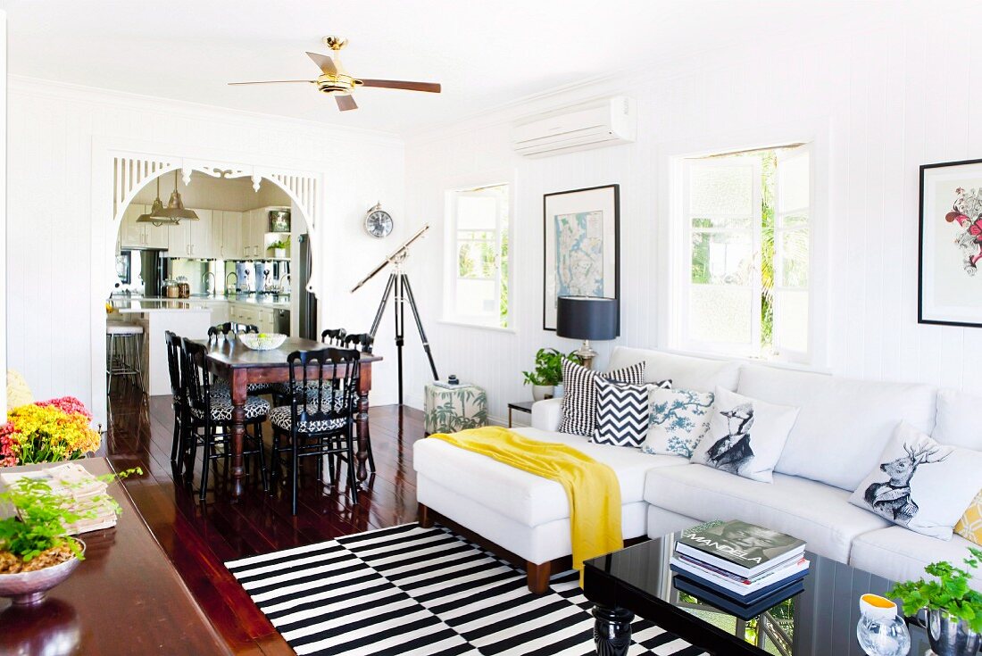 Comfortable, country-house living area with black and white striped rug, white sofa, dining area and view into kitchen