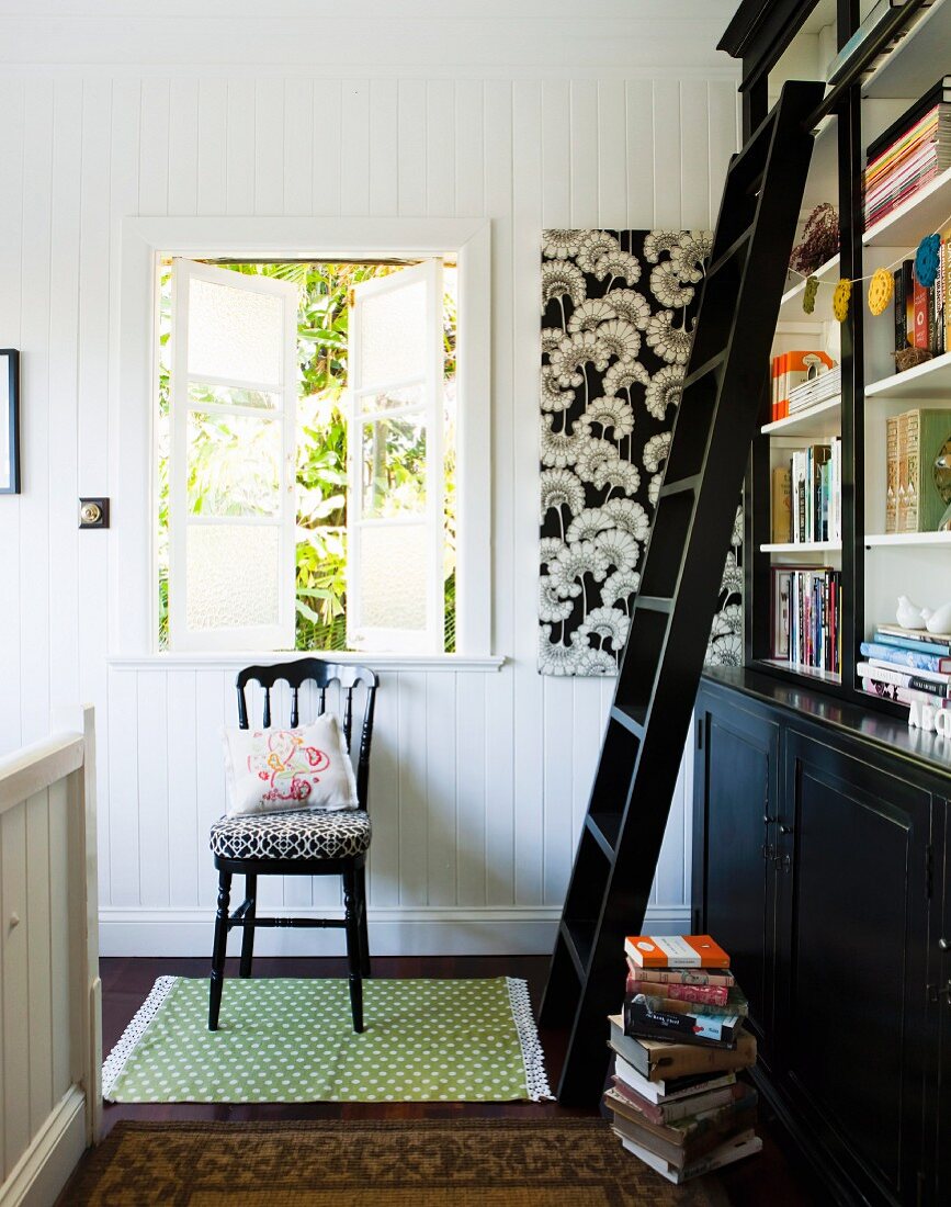 Dark brown bookcase with library ladder in front of open lattice window and wooden, country-house-style chair