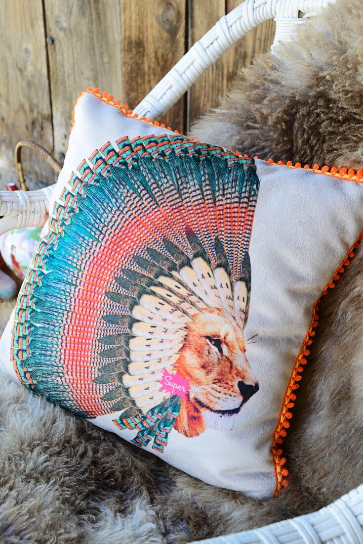 Scatter cushion with motif of lion wearing Native American headdress on cosy sheepskin blanket on wicker chair