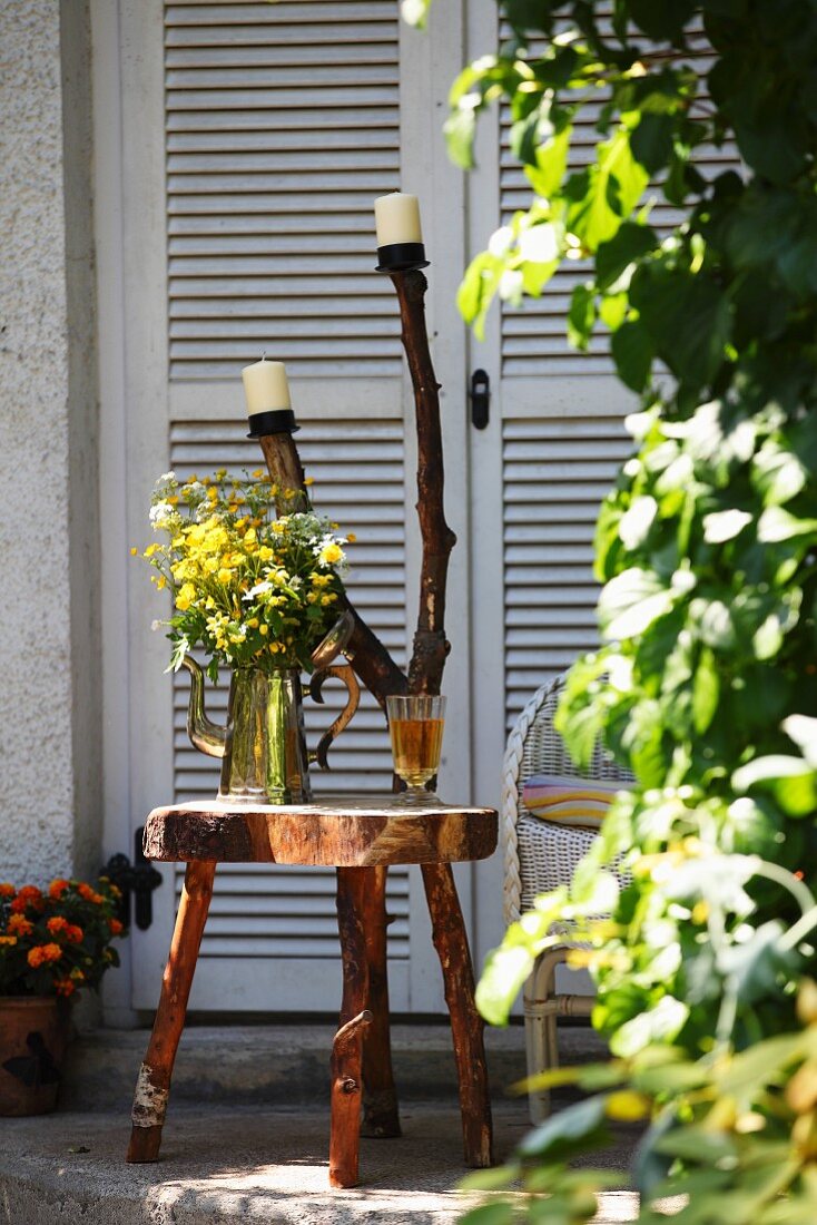 Hand-crafted, rustic side table made from slice of tree trunk on rough branch legs and candlesticks on forked branch