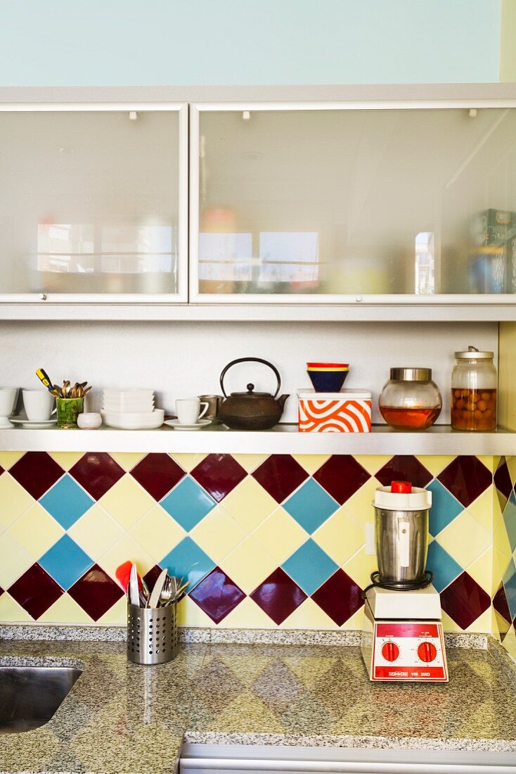 Vintage tiles and granite kitchen worksurface below wall cabinets with frosted glass fronts