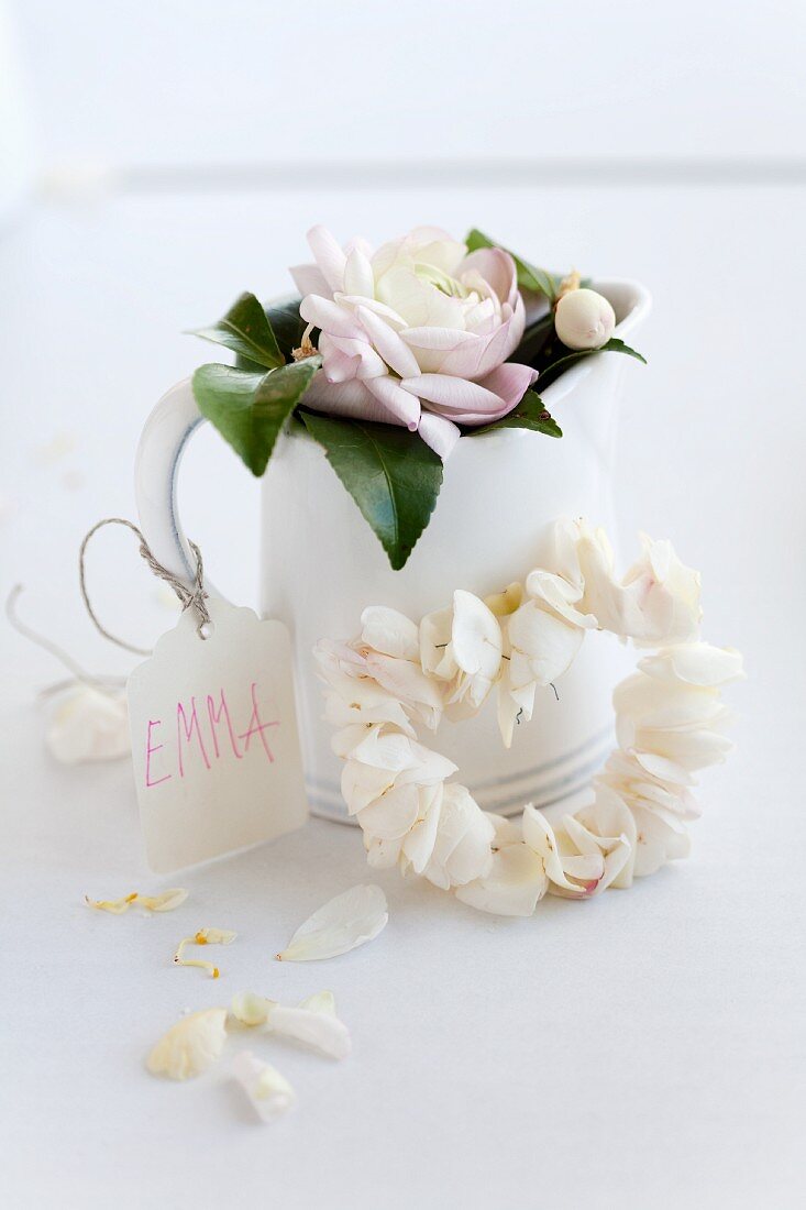 Wreath of threaded camellia petals against jug decorated with name tag and flower