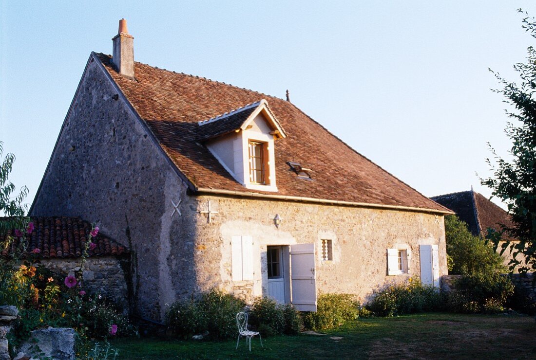 Altes, französiches Bauernhaus mit weissen Fensterläden an einstöckiger, schlichter Natursteinfassade