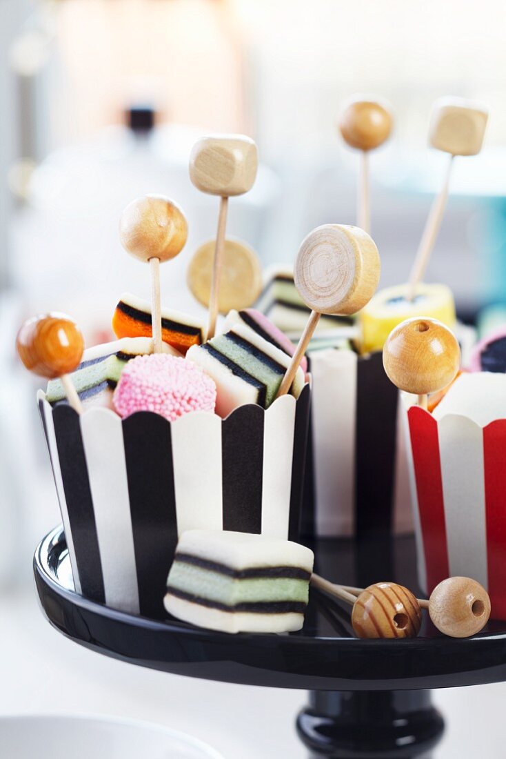 Wooden beads on toothpicks in striped cupcake cases of liquorice allsorts