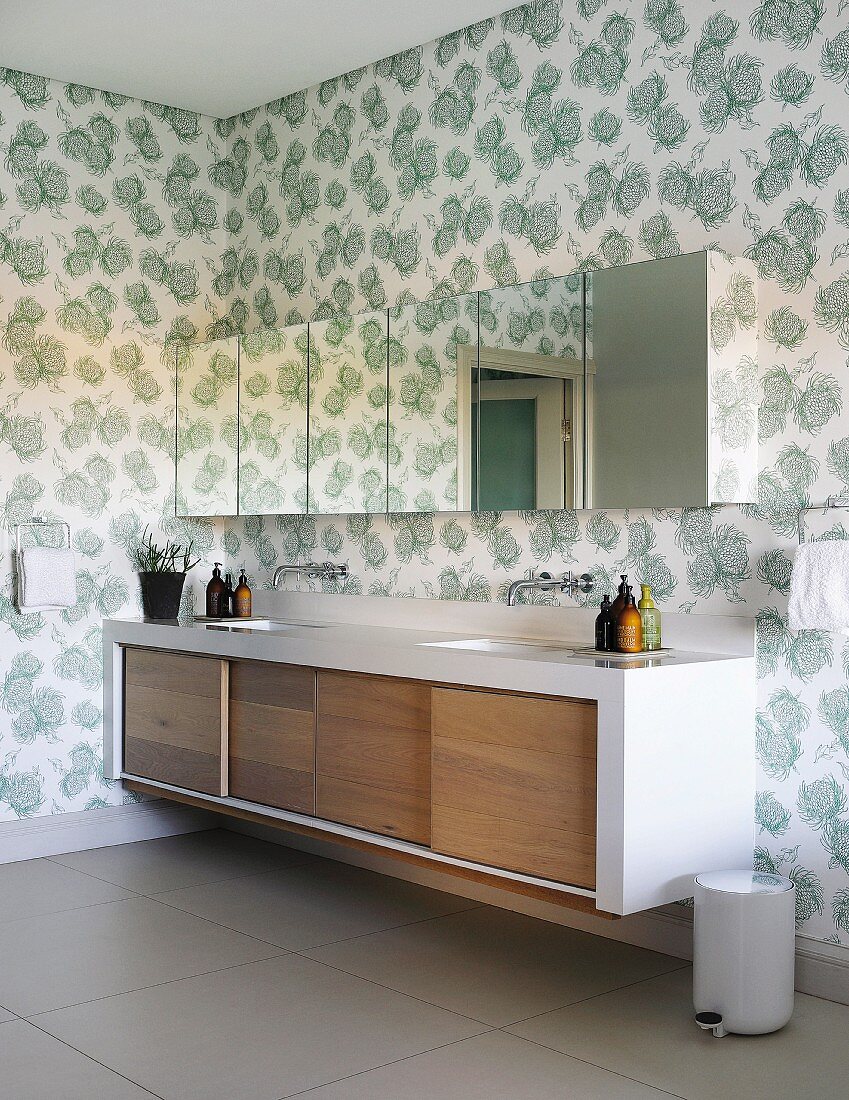 Waschtischzeile mit Holz-Schiebetüren an Unterschränken und Hängeschränke mit Spiegelfront an tapezierter Wand mit floralem Muster