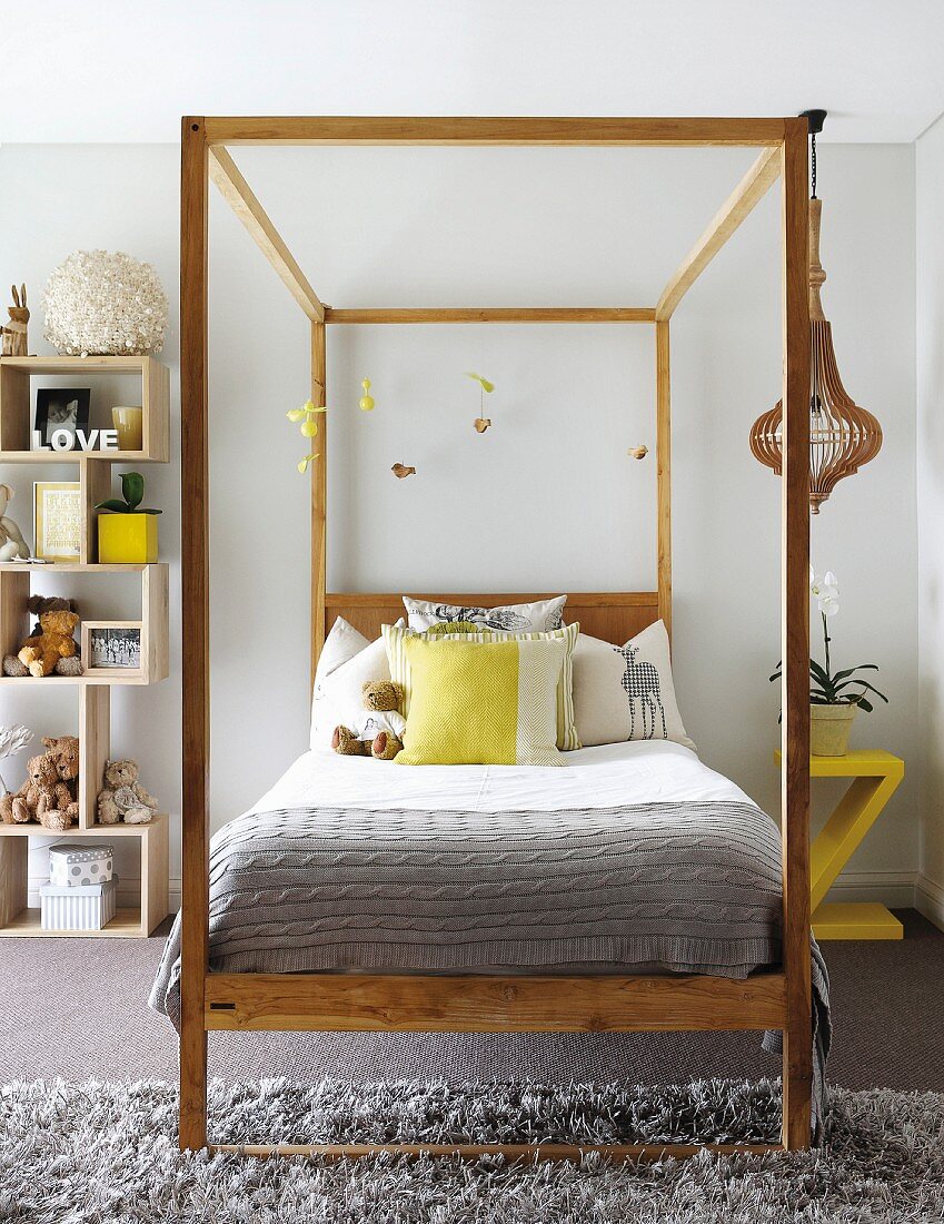 Himmelbett mit Kissen und Holzgestell mit aufgehängtem Mobile, daneben modernes Holzregal mit Stofftieren in Jugendzimmer mit verschiedenen grauen Teppichen
