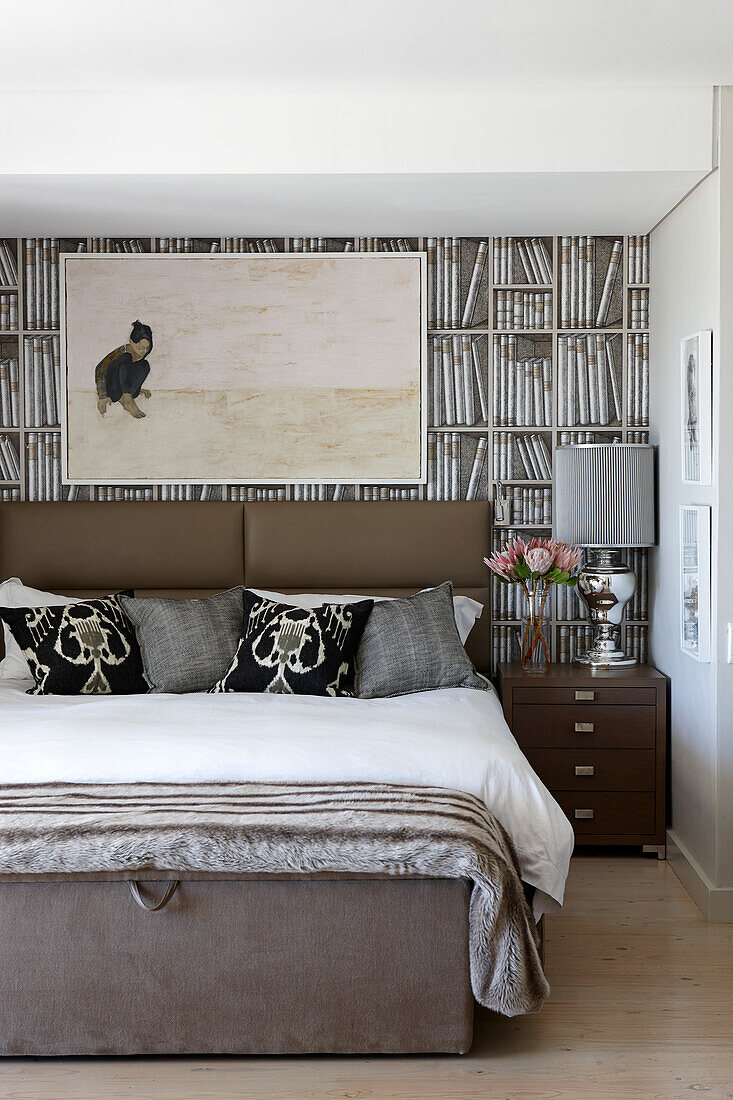 Double bed with high headboard and painting above with book wallpaper