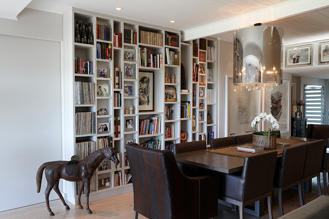 Table with dark leather stools in front of wall of books and horse statue