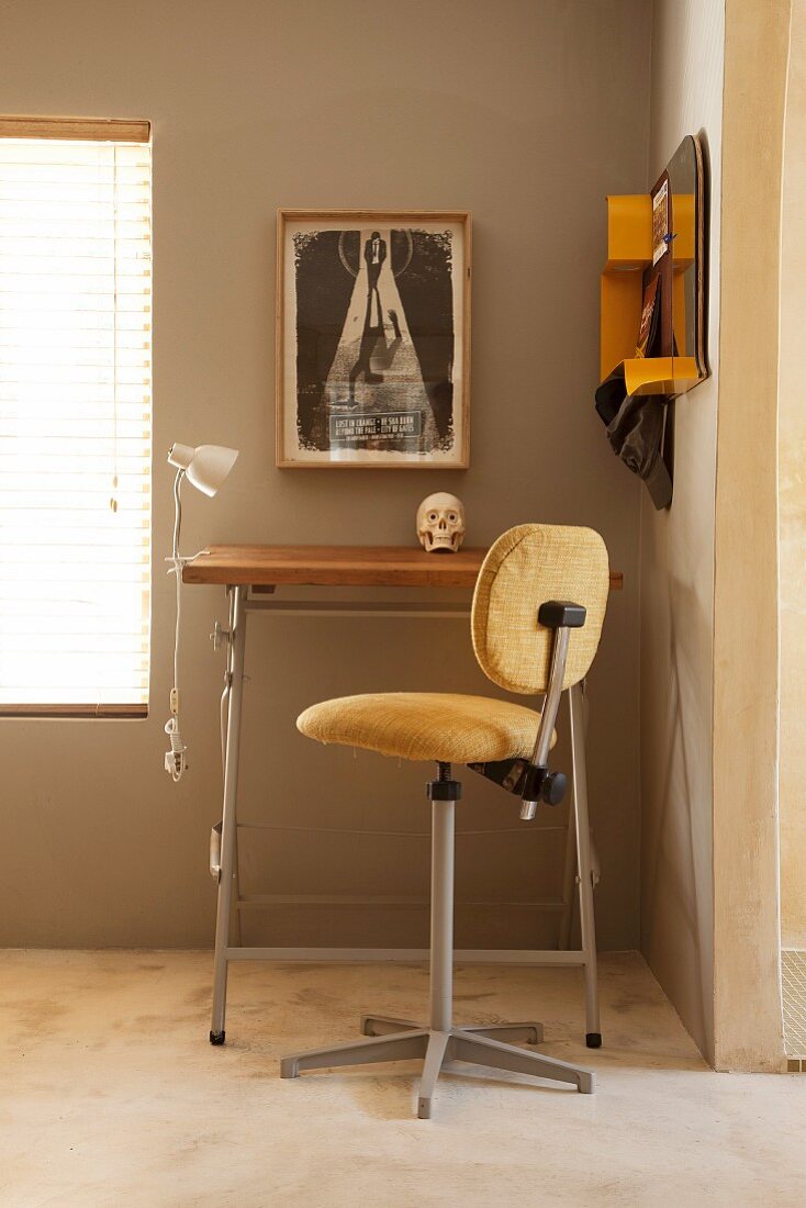 Stehhilfe mit gepolsterter Sitz- und Rückenfläche vor Stehpult an sandfarbener Wand, neben Fenster mit geschlossener Jalousie