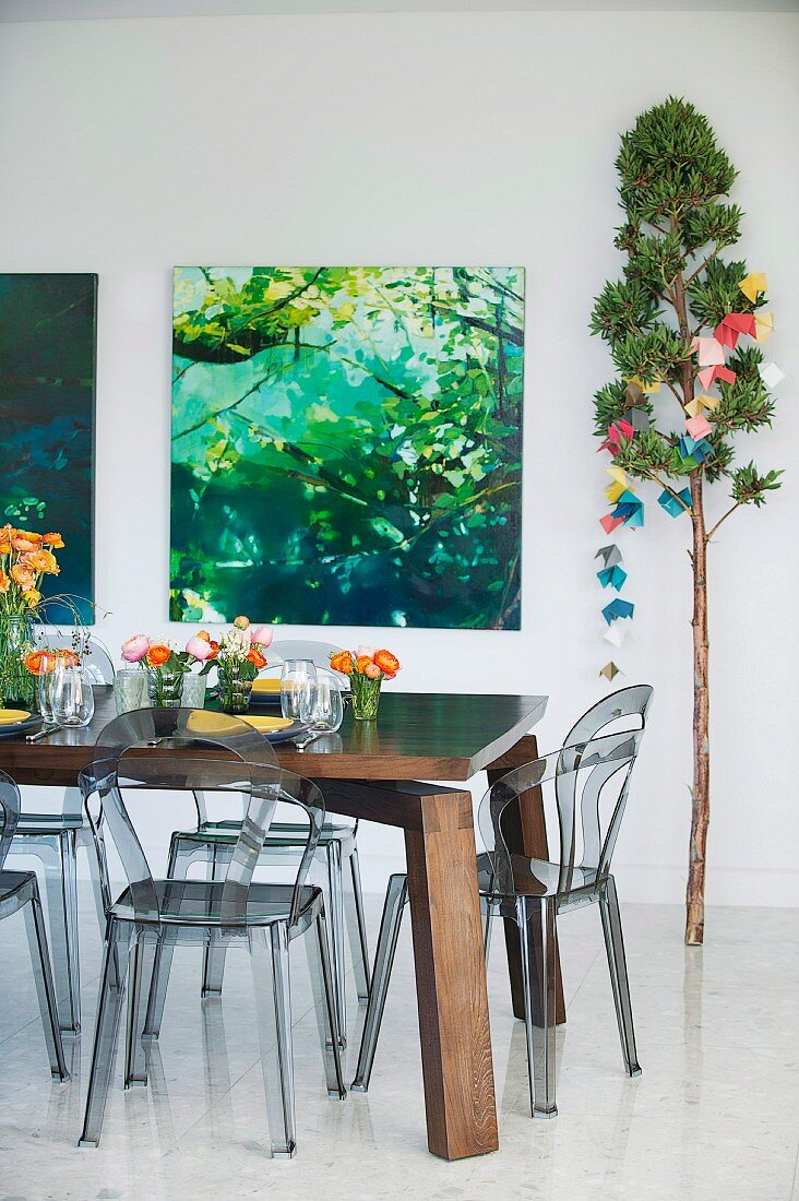 Flower arrangements on solid wooden table and smoked plastic chairs; photos of plants and large branch decorated with origami Christmas garland