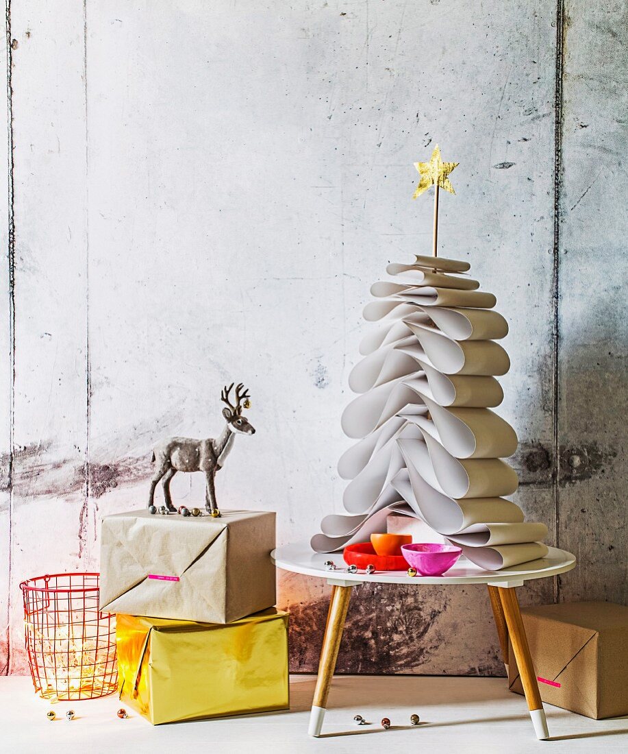 White construction paper Christmas tree held together by dowel with gold star on top on small 50s table next to wrapped present and stag figurine