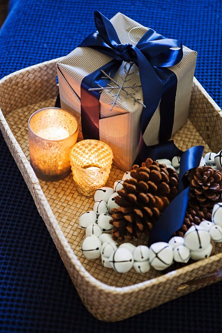 Weihnachtspäckchen, Teelichter & Kranz aus Glöckchen und Zapfen auf Korbtablett