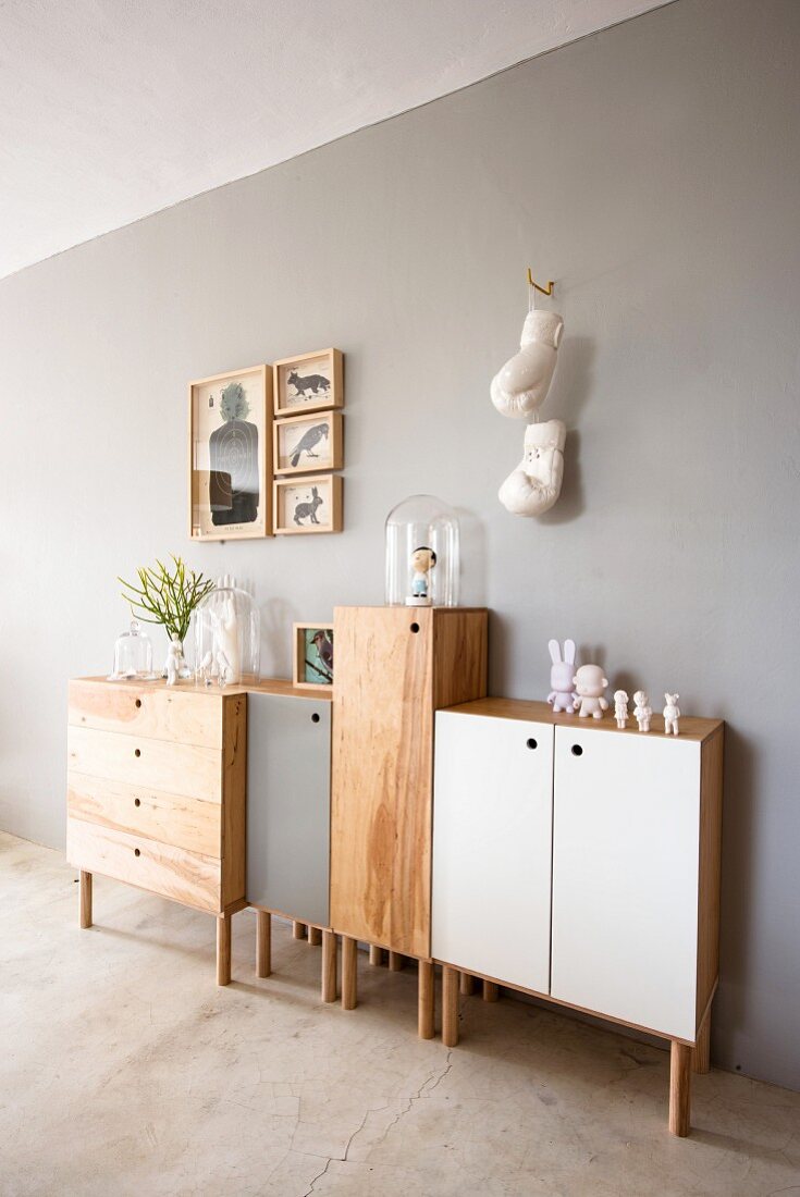 Half-height, wooden console cabinets, some with coloured doors, against wall painted pale grey
