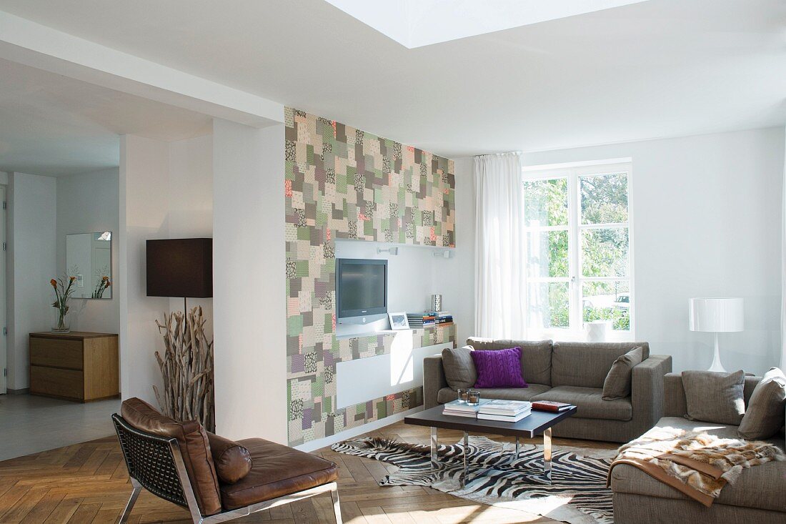 Moderne Sitzgruppe mit Zebrafellteppich vor einer im Patchworkmuster gestalteten Medienwand im offenen Wohnraum