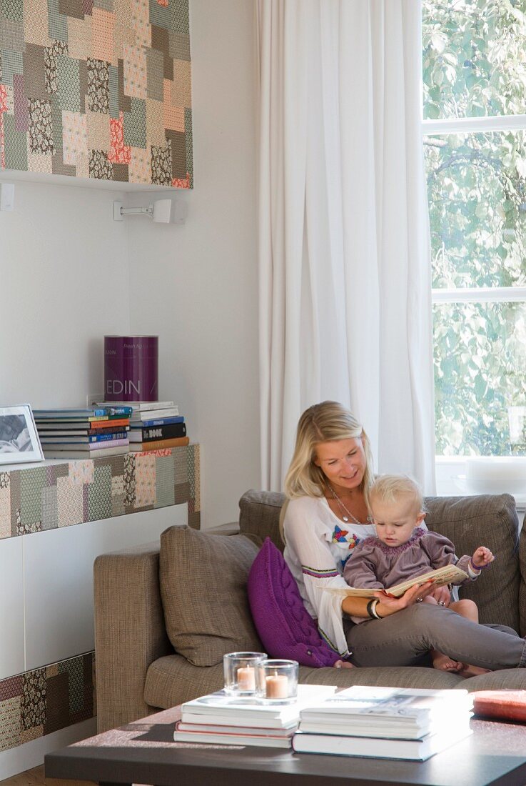 Mutter und Kleinkind beim Vorlesen auf dem Sofa; seitlich Einbauwand mit Patchworkfronten