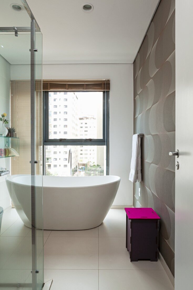 Purple bin lid as splash of colour in elegant, modern white bathroom with free-standing bathtub and dynamic pattern on wall