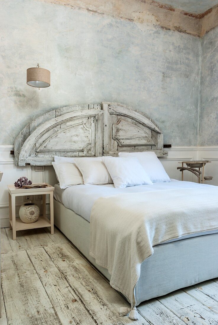 Weiß antikes Schlafzimmer mit marmorierter Wandgestaltung und abgenutztem Dielenboden, alte Holzelementen als Kopfteil hinter Doppelbett