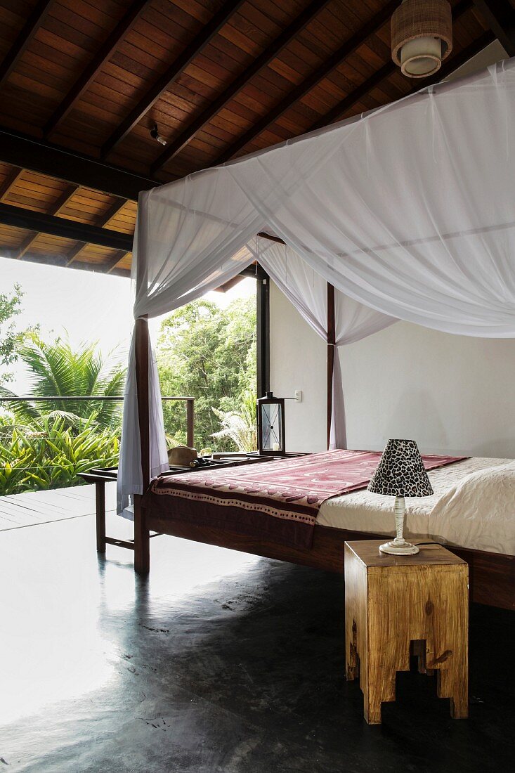Holzbett mit Moskito Baldachin unter offenem Holzdach in tropischer Umgebung
