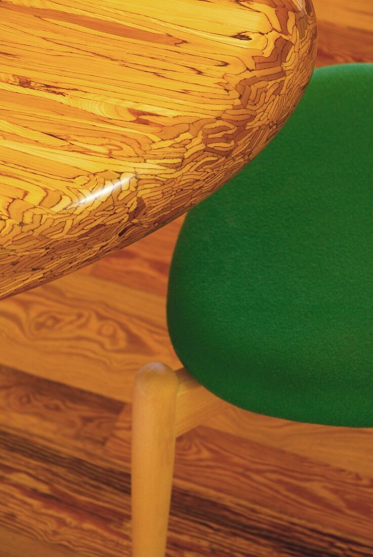 Detail of figured wooden table top and partially visible chair with green seat cushion